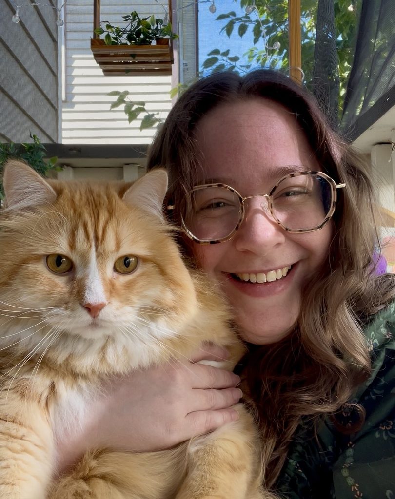 White woman holds orange cat up to face, smiling.